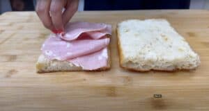 Making a mortadella sandwich on fresh bread on a wooden cutting board.